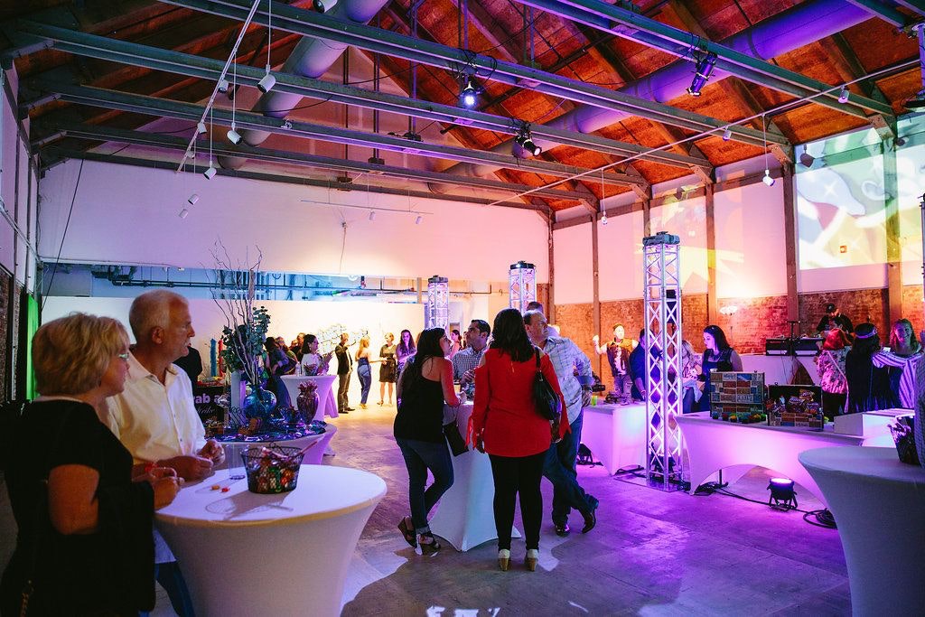 People Stand At Tables In A Room With Colorful Lights