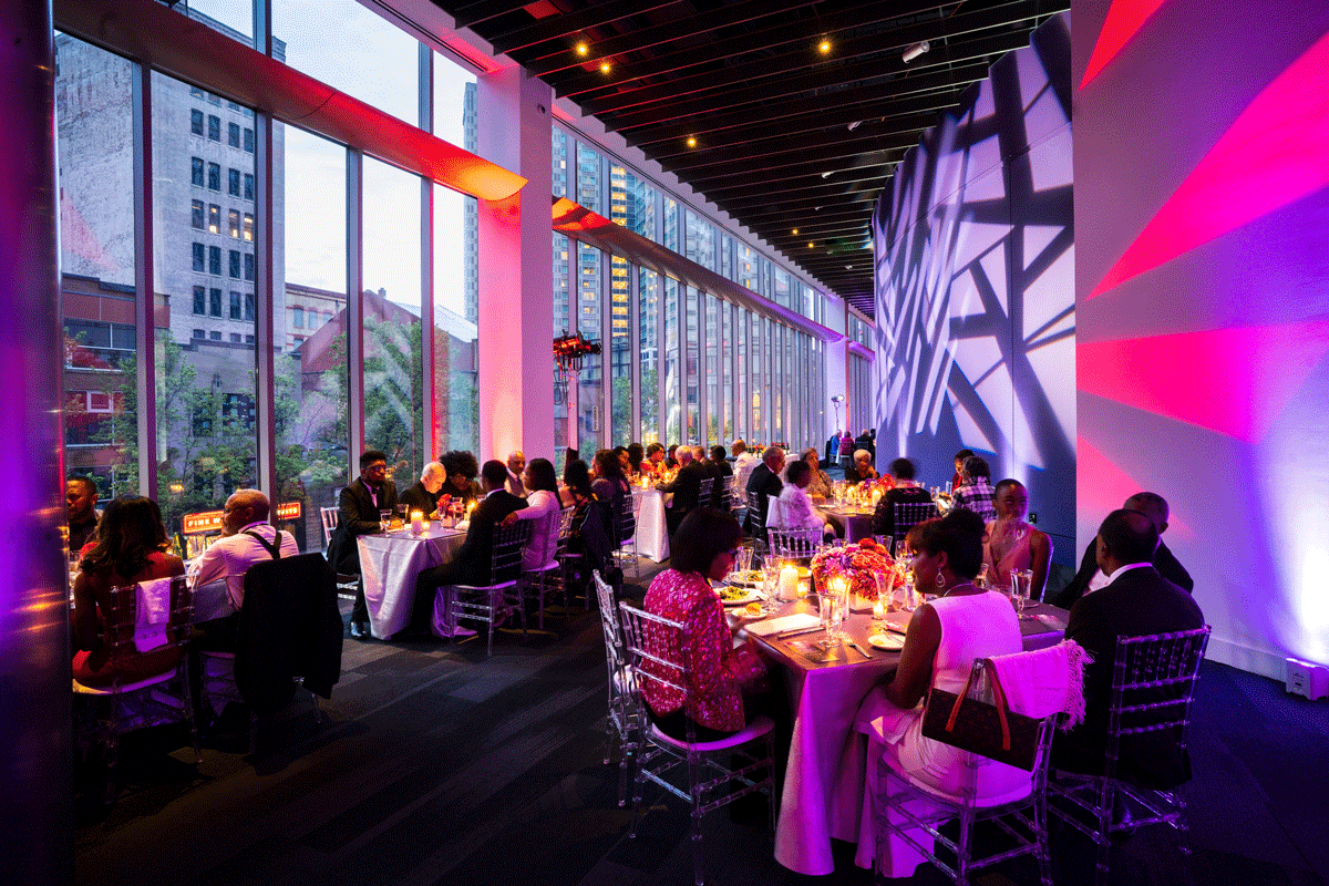 People Are Seated At Tables In A Room With Large Windows And Pink Lights