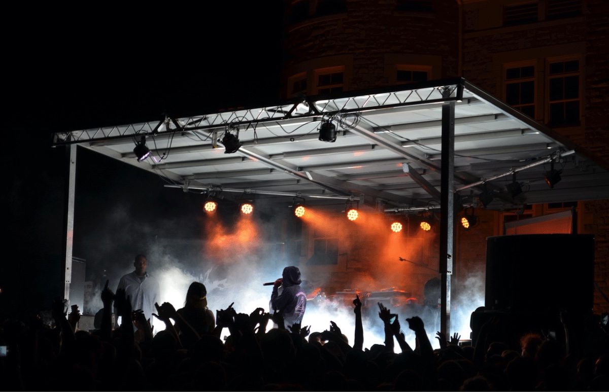 a performer on stage in front of a crowd with a microphone and orange lights