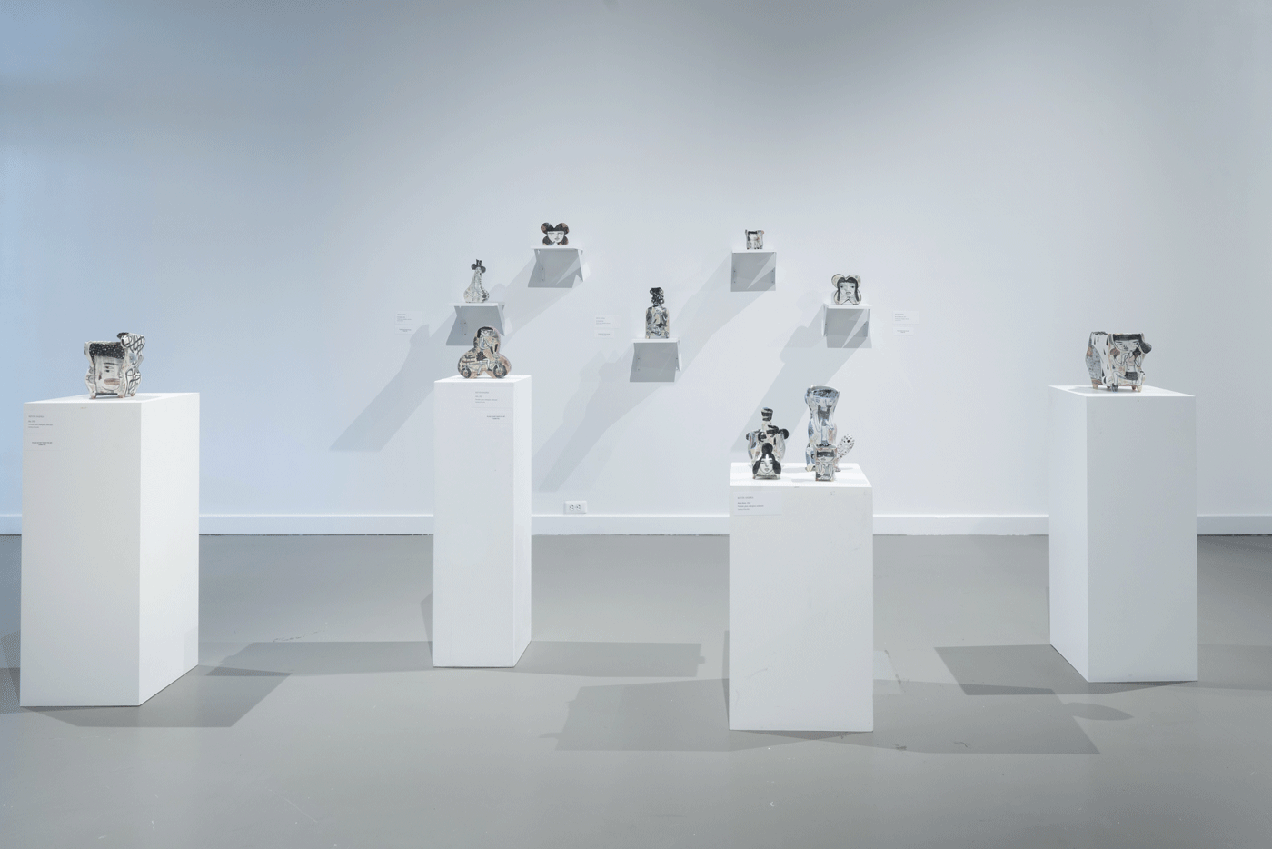 Small sculptures sit on white pedestals and are mounted on the wall
