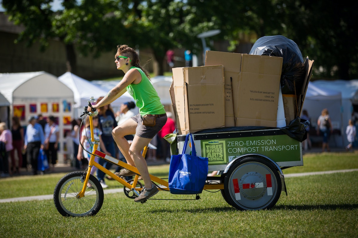 A person rides a bicycle with a trash trailer