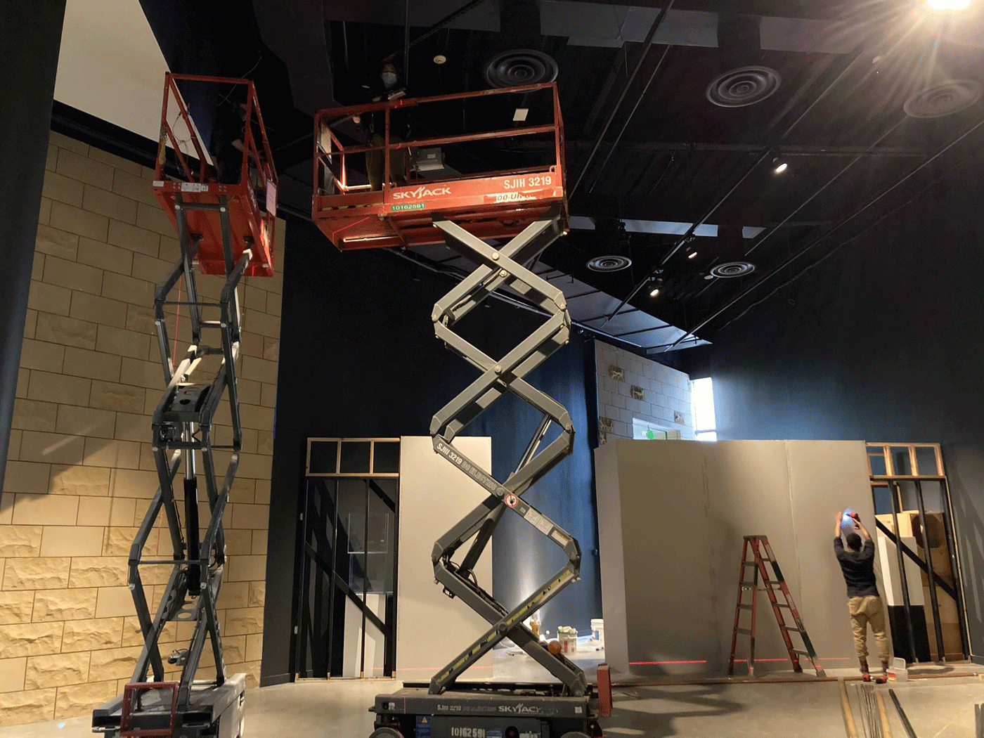 One person drills into a wall while others work from a scissor lift