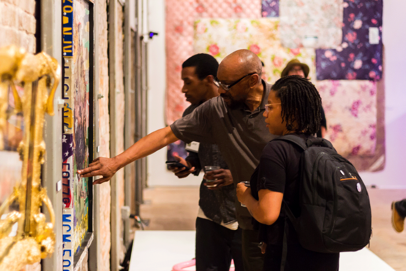 Two People Stand In Front Of And Point At Artwork On A Wall