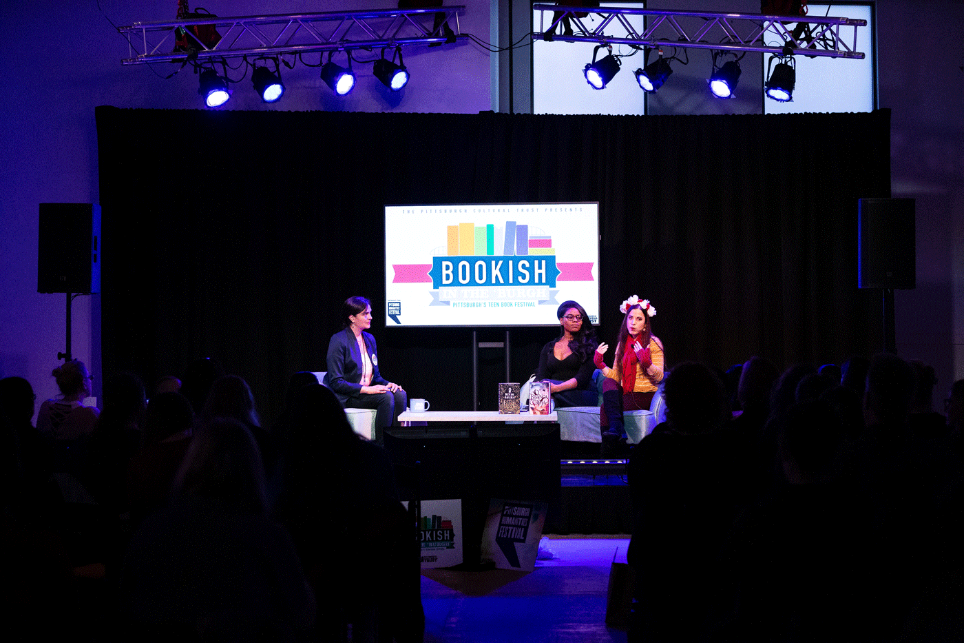 three people sit on a stage with a screen and lights