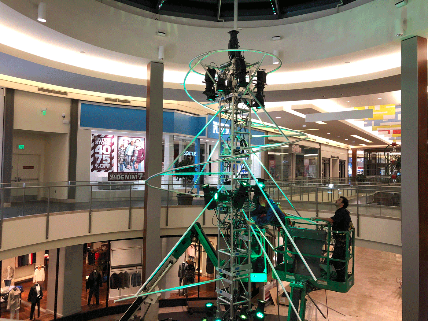 a person on a lift stands amongst a metal structure and green lighting