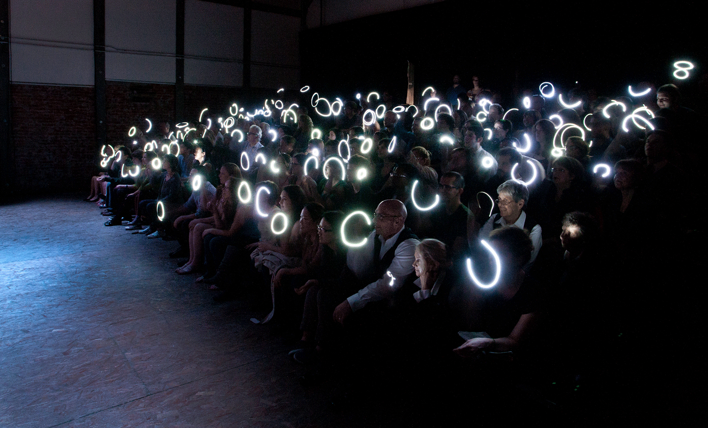 An audience sits in a dark room, each with glowing white rings