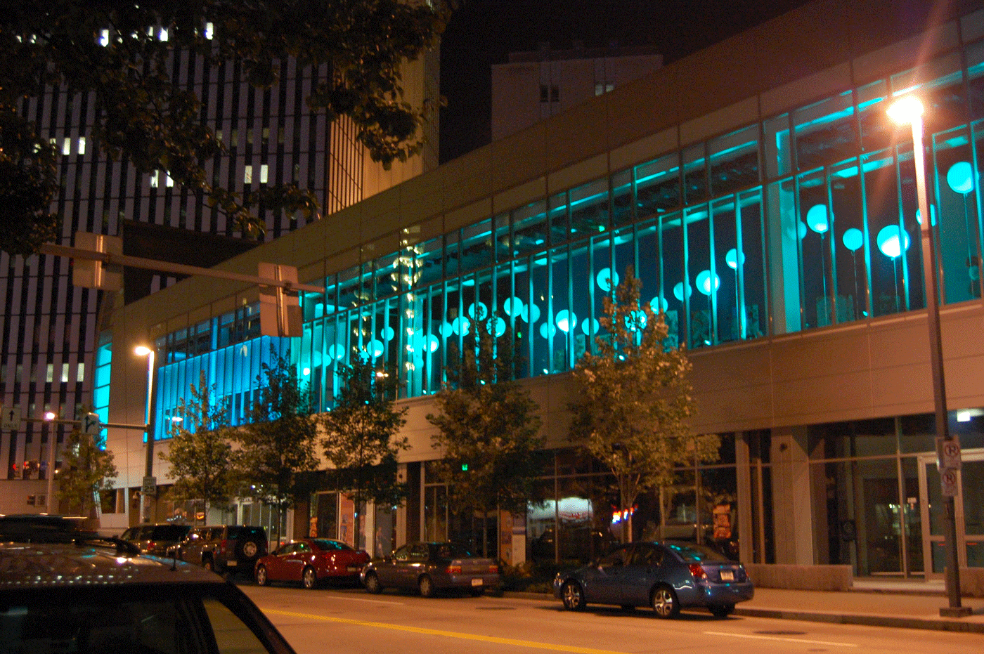 A city building with tall windows is illuminated with blue light and glowing orbs