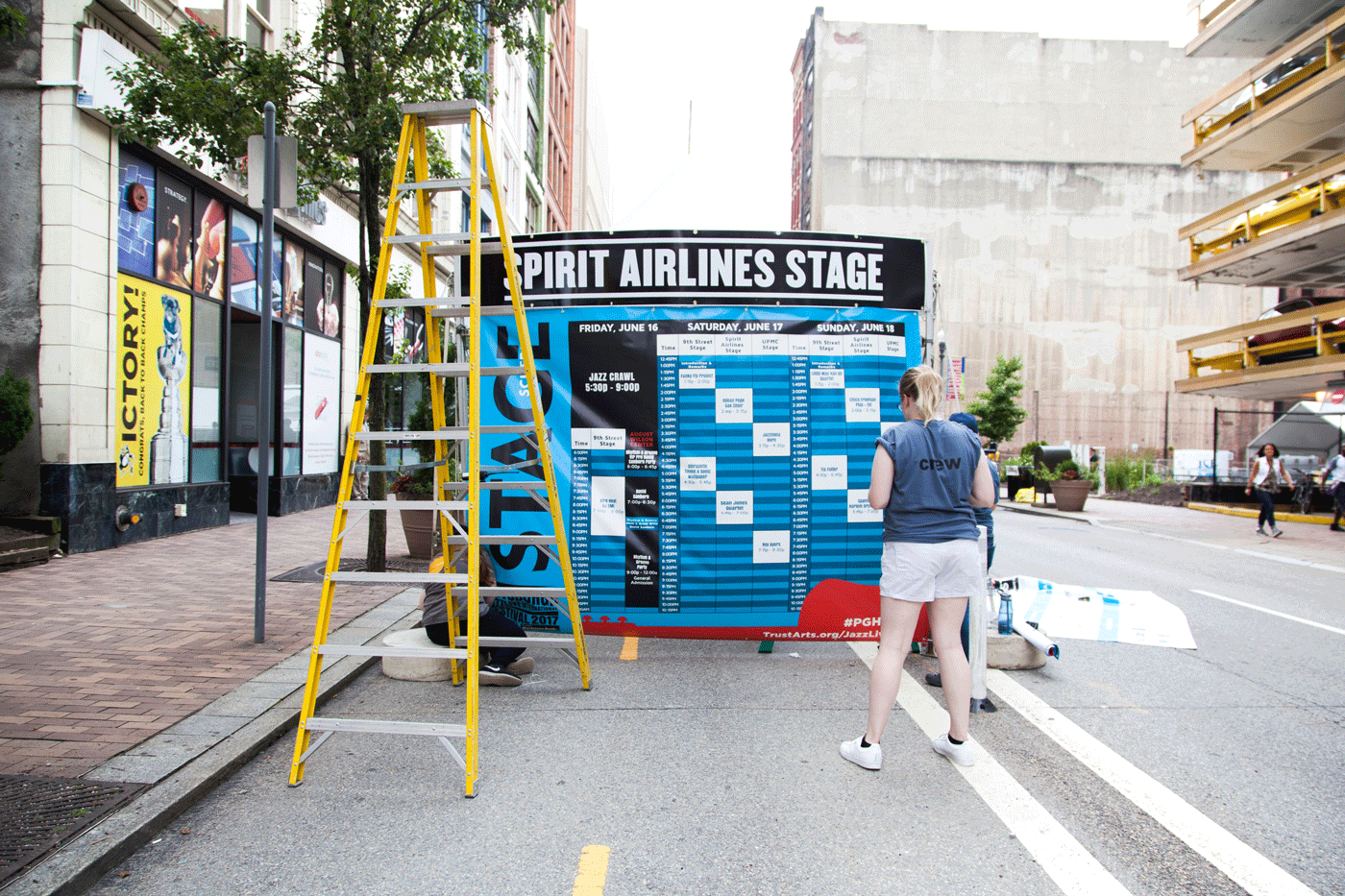 A woman stands towards a stage schedule with a tall yellow ladder