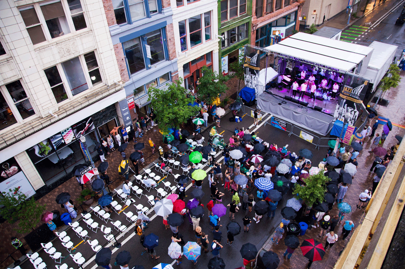 A Crowd With Umbrellas Looks Onto A Stage