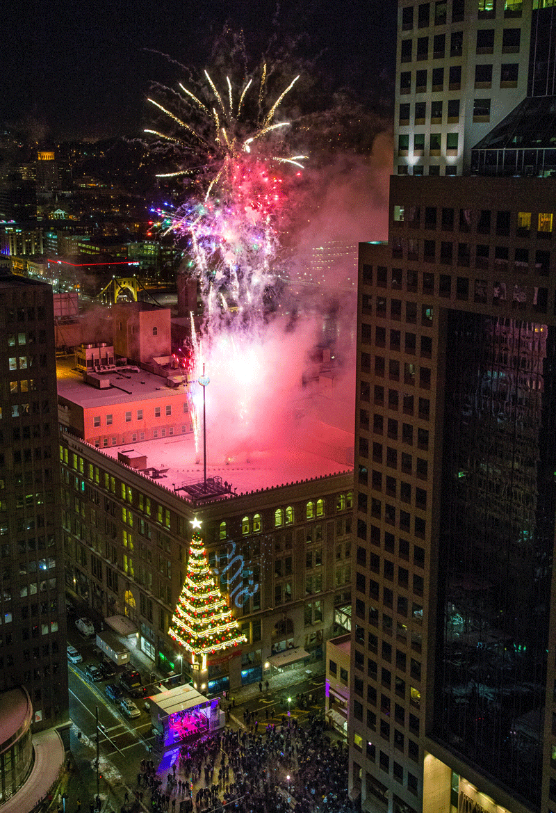 Fireworks explode on a rooftop above a giant Christmas tree
