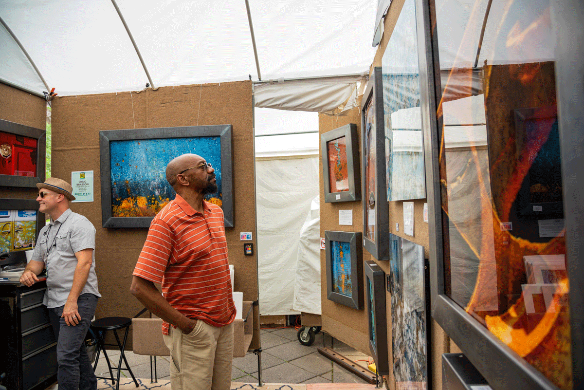 Two men stand in a tent looking at hanging artwork