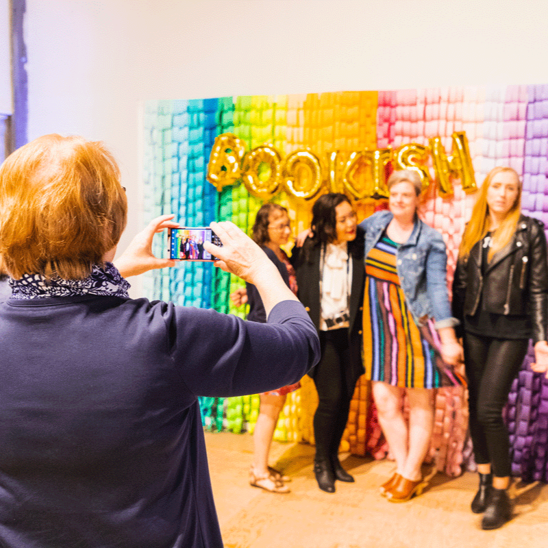 Four people pose for a picture in front of a rainbow background