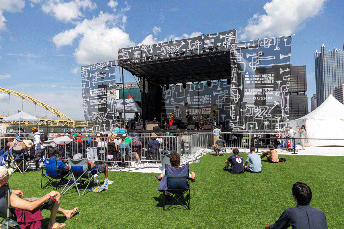 People sit on a lawn looking at a performance on a stage